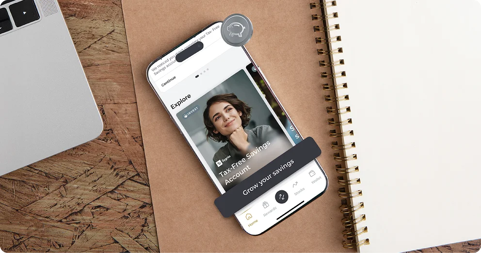 Person holding smartphone showing Kastelo app with TFSA investment, laptop and notebook on desk