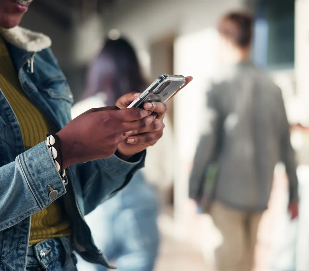 A young woman checking her investments on her phone while walking through a campus corridor
